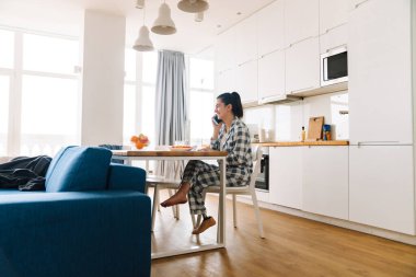 Protezli genç bir kadın evde kahvaltı ederken cep telefonuyla konuşuyor.