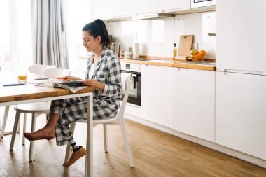 Protezli genç bir kadın evdeki mutfakta otururken ödev yapıyor.
