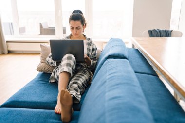Protezli genç bir kadın evdeki kanepede dinlenirken dizüstü bilgisayar kullanıyor.