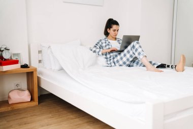 Protezli genç bir kadın evde yatarken dizüstü bilgisayar kullanıyor.