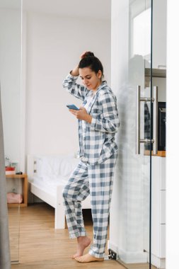 Protezli genç bir kadın evde dururken cep telefonu kullanıyor.