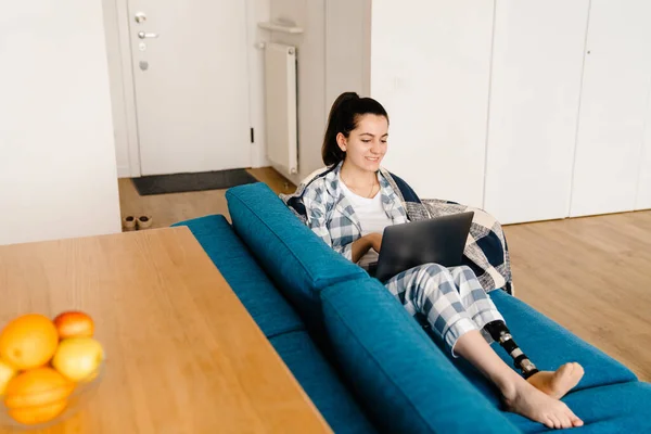 Protezli Genç Bir Kadın Evdeki Kanepede Dinlenirken Dizüstü Bilgisayar Kullanıyor — Stok fotoğraf
