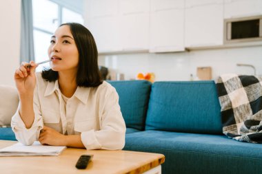 Hoş, düşünceli Asyalı kadın evdeki rahat, ferah oturma odasına notlar yazıyor.