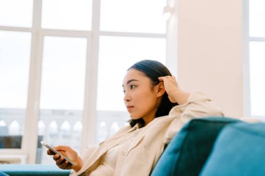 Genç, güzel Asyalı bir kız. Saçlarını düzeltip evdeki rahat, ferah oturma odasında koltukta oturuyor.