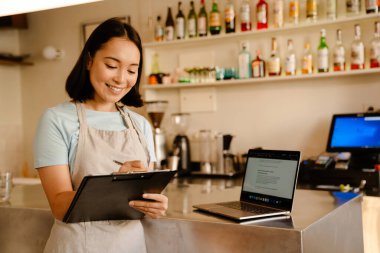 Genç Asyalı barista kadın kafede çalışırken notlar yazıyor.