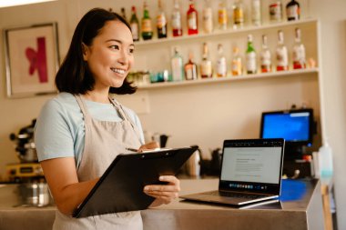 Genç Asyalı barista kadın kafede çalışırken notlar yazıyor.