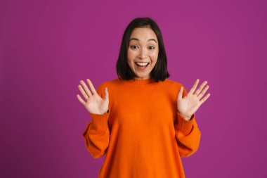 Heyecanlı Asyalı kadın avuçlarını mor arka planda izole halde gösterirken gülüyor.