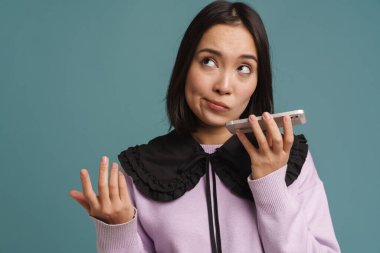 Genç Asyalı kadın mavi arka planda izole edilmiş bir şekilde cep telefonuyla konuşuyor.