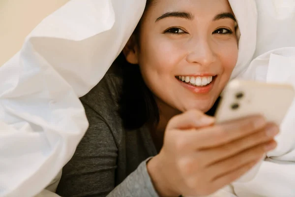 Joven Sonriente Chica Asiática Traje Casa Acostado Con Teléfono Cama — Foto de Stock