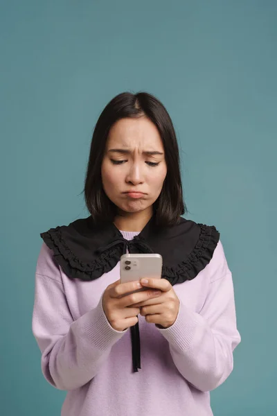 Молодая Азиатская Женщина Хмурясь Используя Мобильный Телефон Изолированы Синем Фоне — стоковое фото