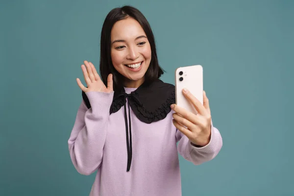 stock image Young asian woman gesturing while taking selfie on cellphone isolated over blue background