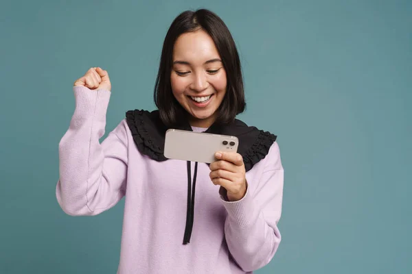 stock image Young asian woman playing online game on mobile phone isolated over blue background