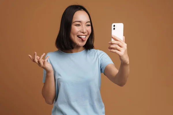 Молода Азіатка Показує Язик Беручи Селфі Мобільний Телефон Ізольовано Бежевому — стокове фото