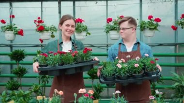 Elinde çiçeklerle gülümseyen kadın serada aşağı sendromlu bir erkek çiçekçiyle.