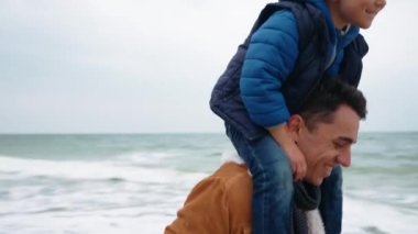 Komik bir baba oğluyla deniz kenarındaki sahilde koşuyor.