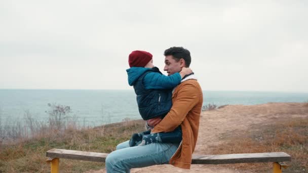 Roztomilý Otec Drží Svého Syna Náručí Objímají Lavičce Moře — Stock video