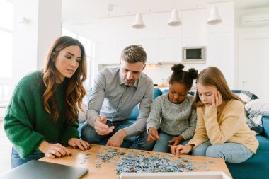 Evlatlık Afrikalı küçük bir kız evdeki oturma odasında ailesiyle bulmaca çözüyor. Evlat edinme kavramı.