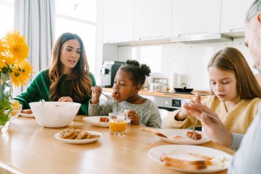 Afrikalı evlat edinilmiş küçük kız evde ailesiyle berakfast yiyor. Evlat edinme kavramı.