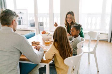Evlatlık afro kızla mutlu bir aile evdeki rahat mutfakta kahvaltı ediyorlar. Evlat edinme kavramı.