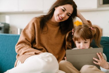 Beyaz kız annesiyle evde vakit geçirirken tablet bilgisayar kullanıyor.