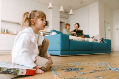 Beyaz sarışın kız evde ailesiyle vakit geçirirken bulmacayı tamamlıyor.