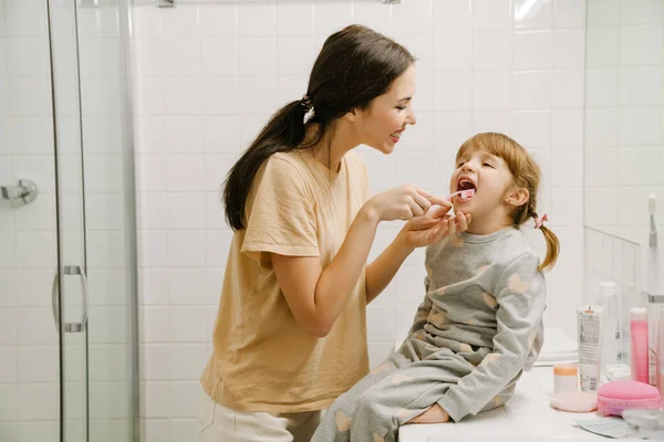 White woman brushing her daughter\'s teeth in bathroom at home