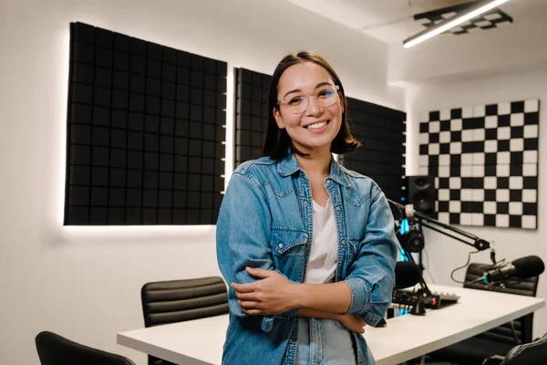 Beautiful happy young female radio host smiling while broadcasting in studio