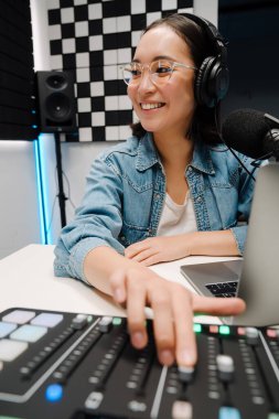 Stüdyoda yayın yaparken kulaklık ve ses karıştırıcı kullanan güzel, mutlu, genç bir radyo sunucusu.