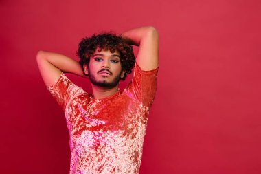 Makyajlı genç kıvırcık adam pembe arka planda izole edilmiş kameraya bakıyor.