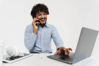 Yetişkin Hintli ofis çalışanı. Gri arka planda bilgisayarla gülümsüyor ve konuşuyor.