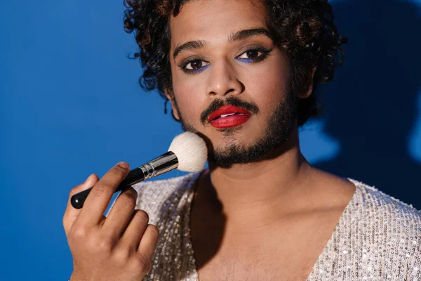 stock image Young curly man using powder brush and looking at camera isolated over blue background