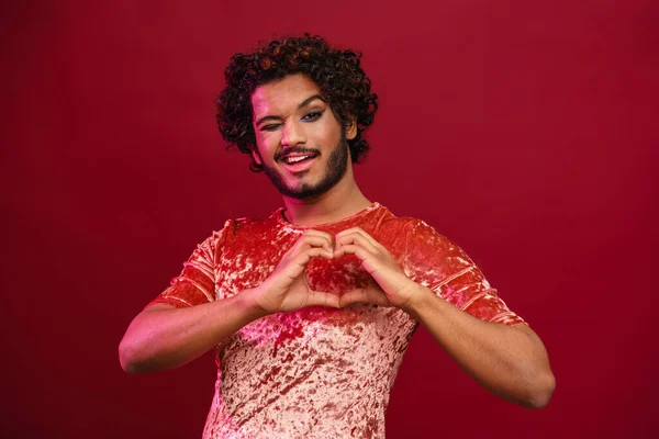 Young Curly Man Makeup Winking While Making Heart Gesture Isolated — Stock Photo, Image
