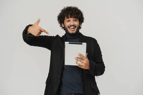 stock image Adult young indian handsome smiling curly man pointing on tablet over isolated grey background