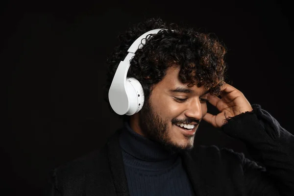 stock image Portrait of young indian curly smiling man in headphones looking downwards over isolated dark background