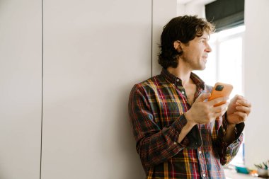 Beyaz adam evde dururken gülümsüyor ve cep telefonu kullanıyor.