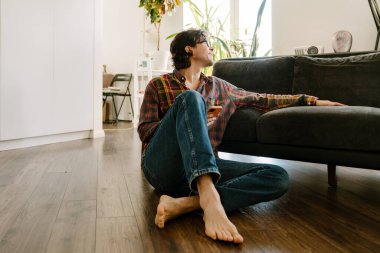 Gözlüklü beyaz adam evde otururken cep telefonu kullanıyor.