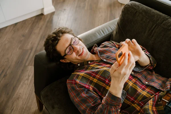 Bílý Muž Úsměvem Pomocí Mobilního Telefonu Zatímco Odpočívá Gauči Doma — Stock fotografie