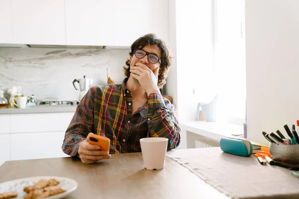 Bílý Muž Směje Používá Mobilní Telefon Zatímco Sedí Doma Kuchyni — Stock fotografie