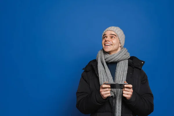 Junger Weißer Mann Winterkleidung Mit Handy Vor Blauem Hintergrund Isoliert — Stockfoto