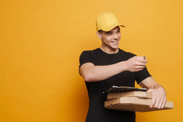 年轻的送货员一边微笑着一边摆姿势 把剪贴板和披萨盒与黄色背景隔离开来 — 图库照片