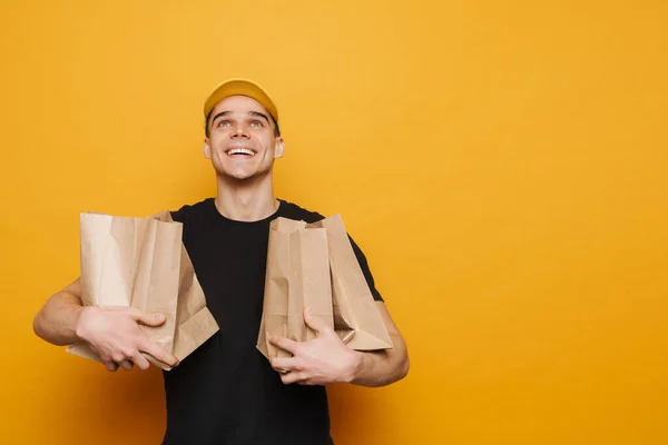 Junger Zusteller Lächelt Während Mit Papiertüten Vor Gelbem Hintergrund Posiert — Stockfoto
