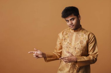 Genç Hintli adam gülümsüyor ve sarı arka planda izole edilmiş parmakları işaret ediyor.