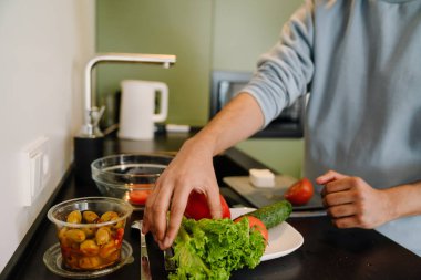 Erkek eli sebze alıp evdeki rahat mutfakta salata pişiriyor.