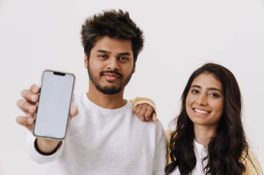 Genç Hintli çift gülerken beyaz arka planda izole edilmiş cep telefonunu gösteriyor.