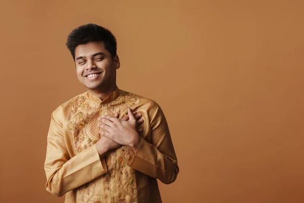 若いインド人男性笑顔と手で彼の心に隔離された上に黄色の背景 — ストック写真