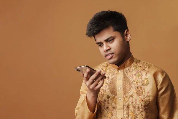 Молодая Брюнетка Индийский Мужчина Держит Глядя Сотовый Телефон Изолированы Желтом — стоковое фото
