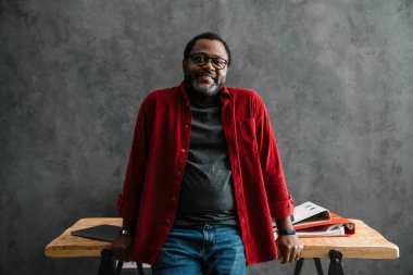 Ofiste çalışırken gülümseyen gözlüklü siyah sakallı adam.