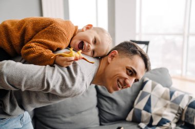 Mutlu beyaz baba gülümsüyor ve evdeki küçük oğlunu sırtında taşıyor.