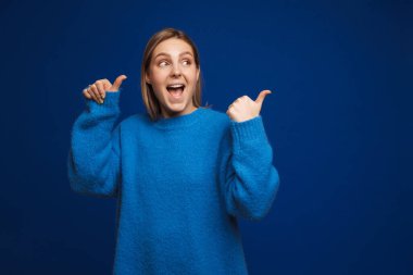 Mavi kazaklı, gülümseyen genç kız mavi izole edilmiş arka planda dikiliyor ve sağa bakıyor.