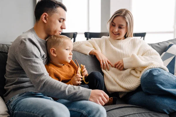 Mutlu beyaz adam ve kadın ve küçük çocuk evdeki kanepede otururken gülümsüyorlar.